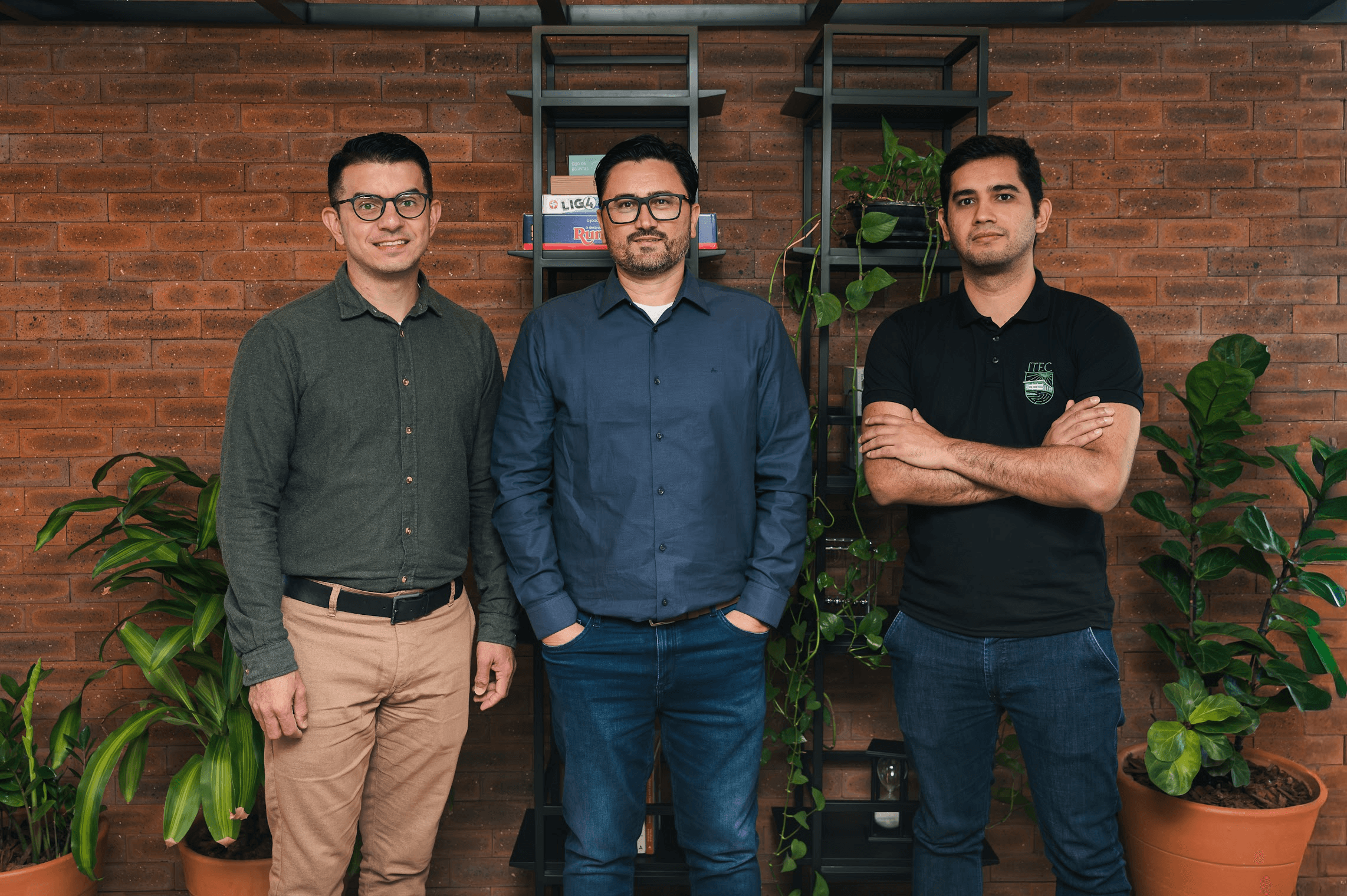 Felipe Domingos da Cunha, Leandro Villas, and Wellington Lobato standing side by side in front of a brick wall.